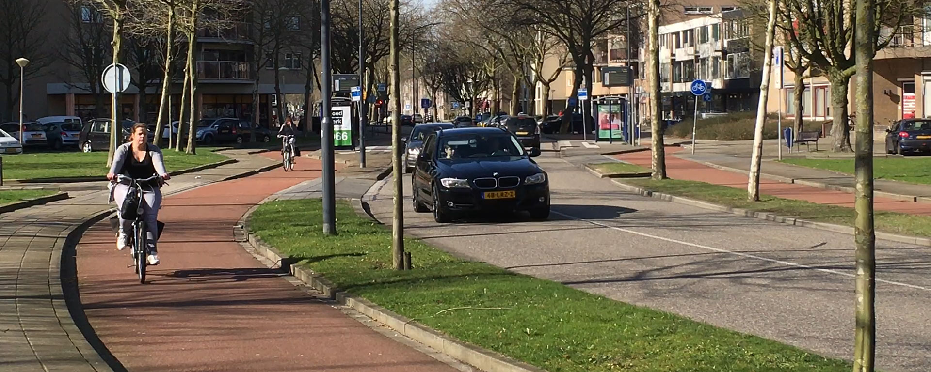 Image of a Dutch street with a protected cycle track on each side. The street has one lane for cars in each direction, and a raised intersection with what looks like a minor side street in the foreground.